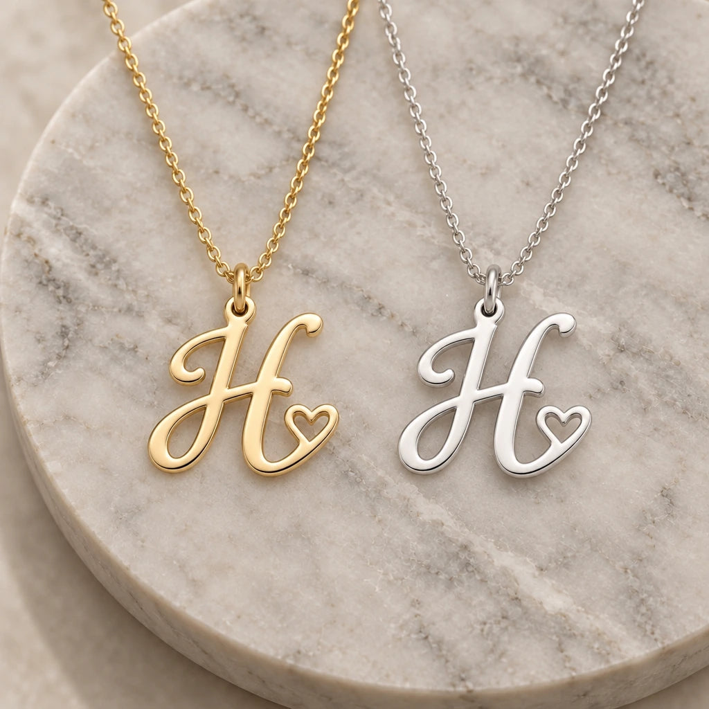 Silver and gold h initial heart pendant necklaces side by side on marble
