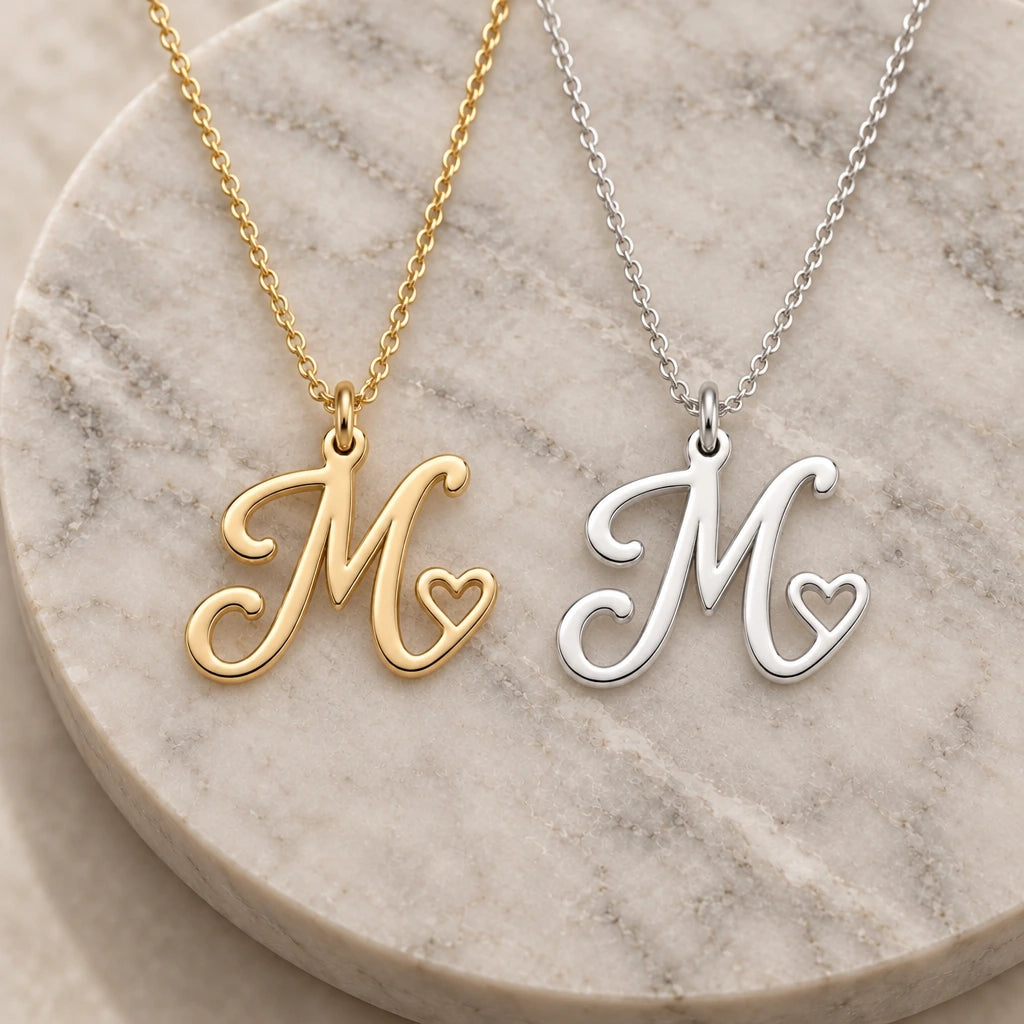 Silver and gold m initial heart pendant necklaces side by side on marble