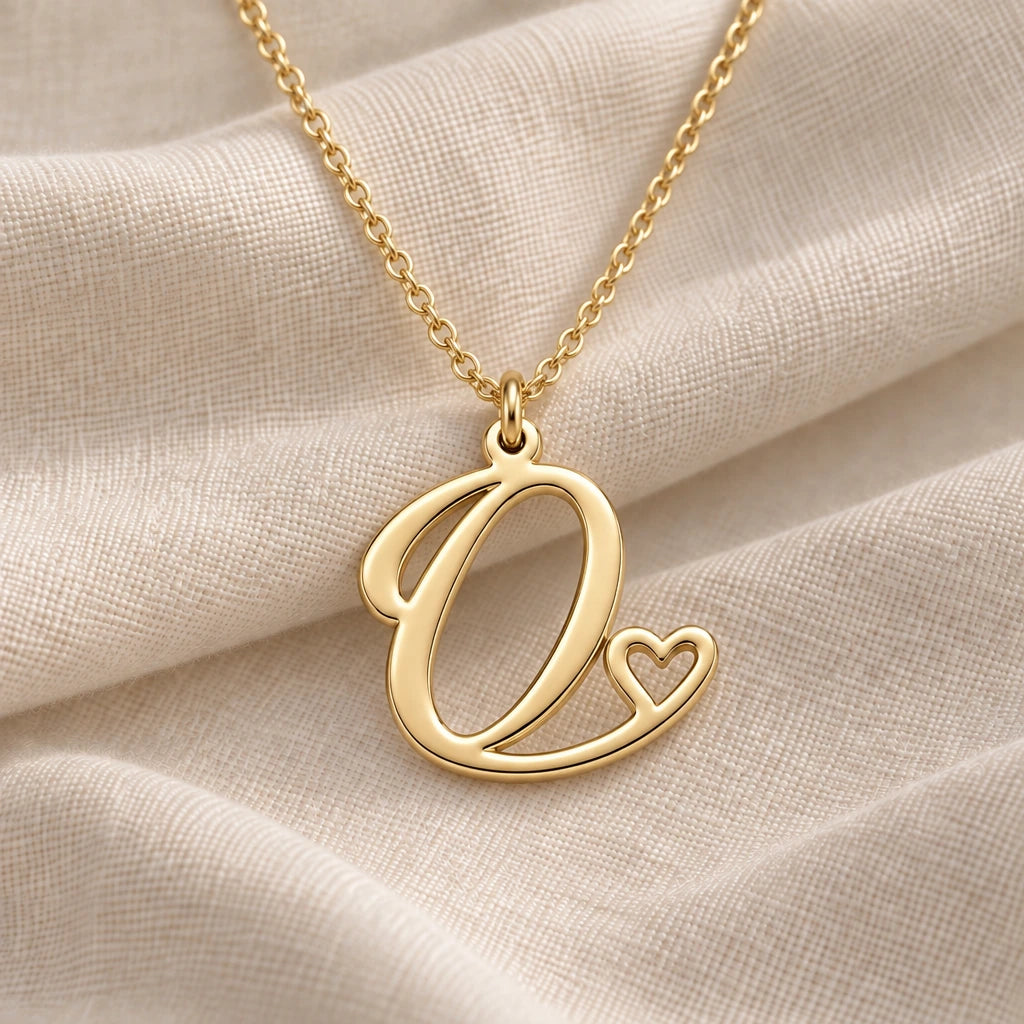 O Initial Heart pendant necklace in a warm gold finish on cream fabric
