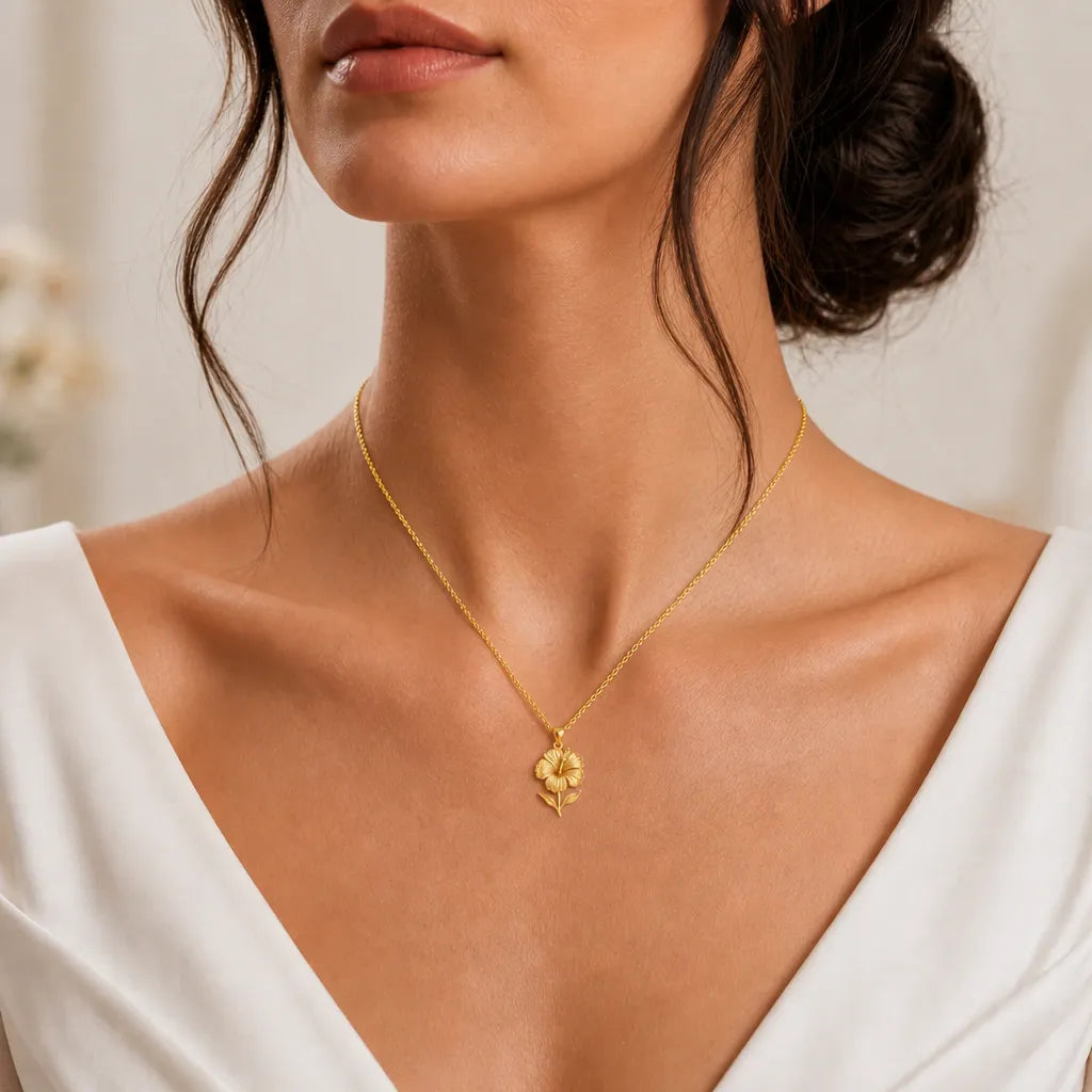 Gold hibiscus flower pendant necklace worn on a model with a white dress, front close-up