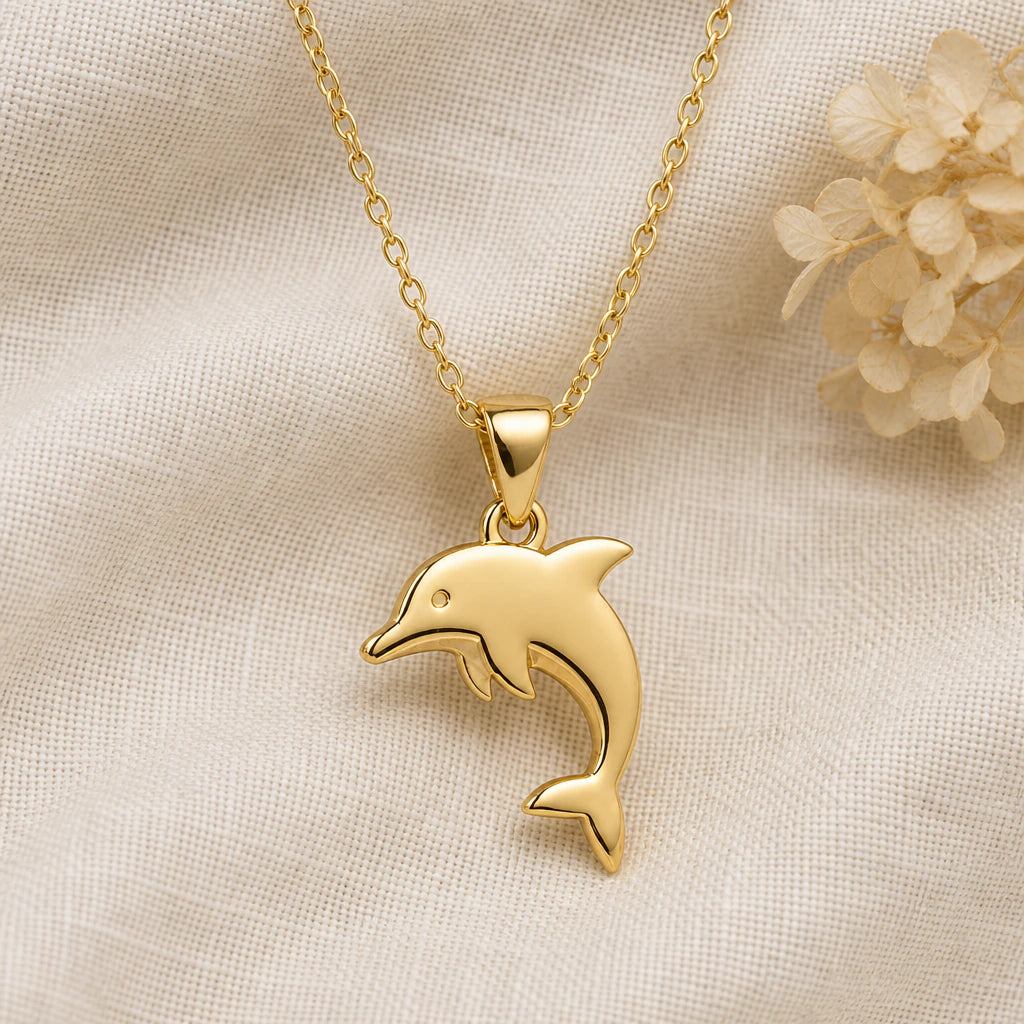 Dolphin pendant necklace in a warm gold finish on cream fabric
