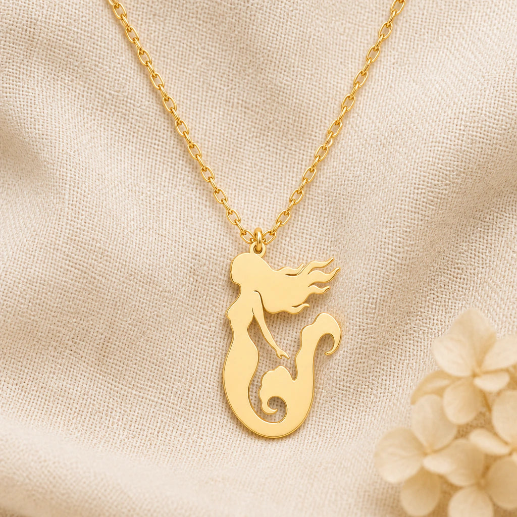 Mermaid pendant necklace in a warm gold finish on cream fabric