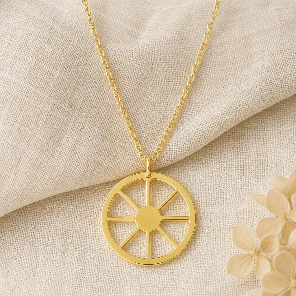 Sun Wheel Symbol pendant necklace in a warm gold finish on cream fabric
