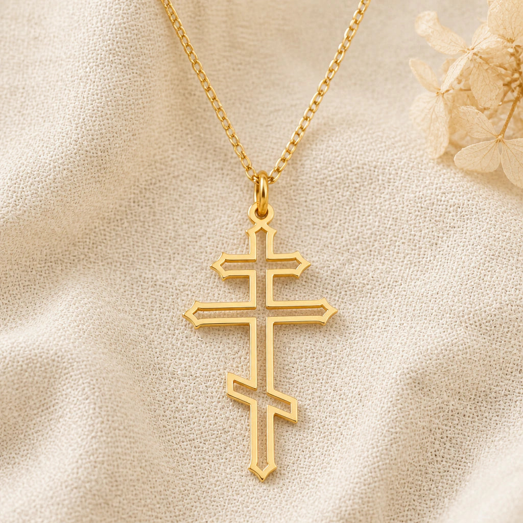 Orthodox Cross pendant necklace in a warm gold finish on cream fabric