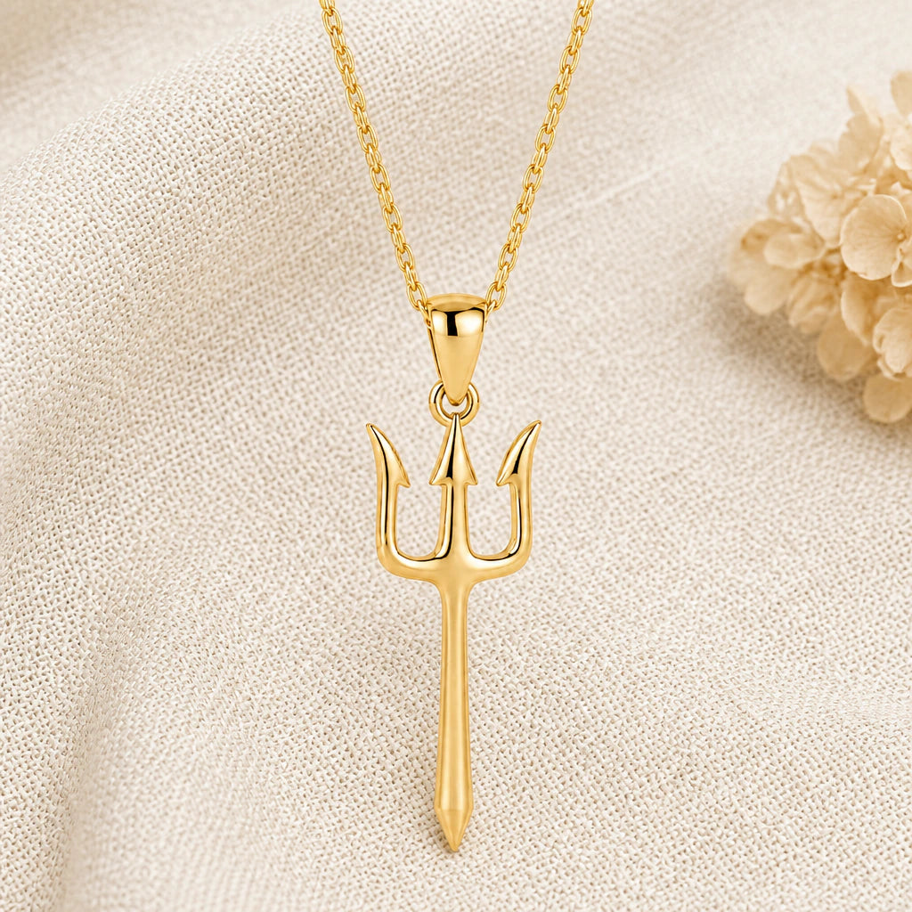 Trident pendant necklace in a warm gold finish on cream fabric