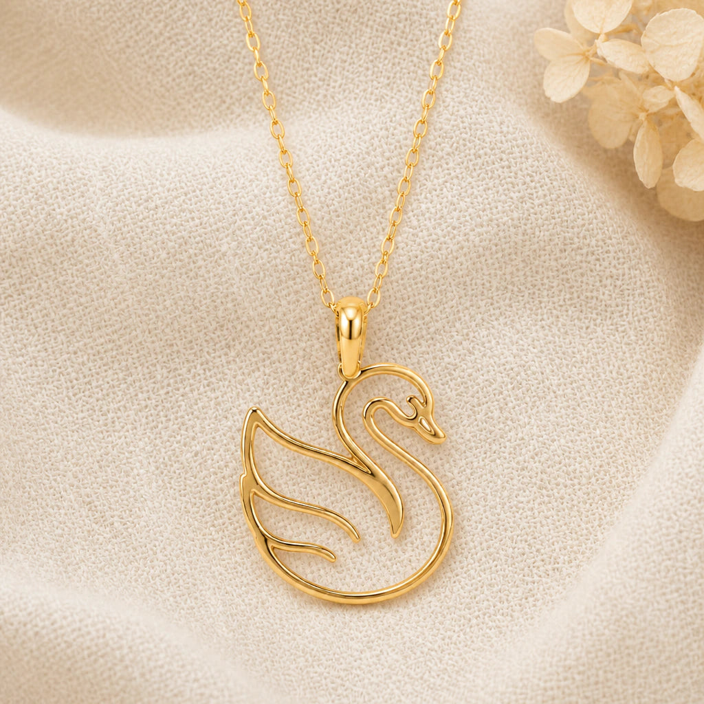 Swan Outline pendant necklace in a warm gold finish on cream fabric