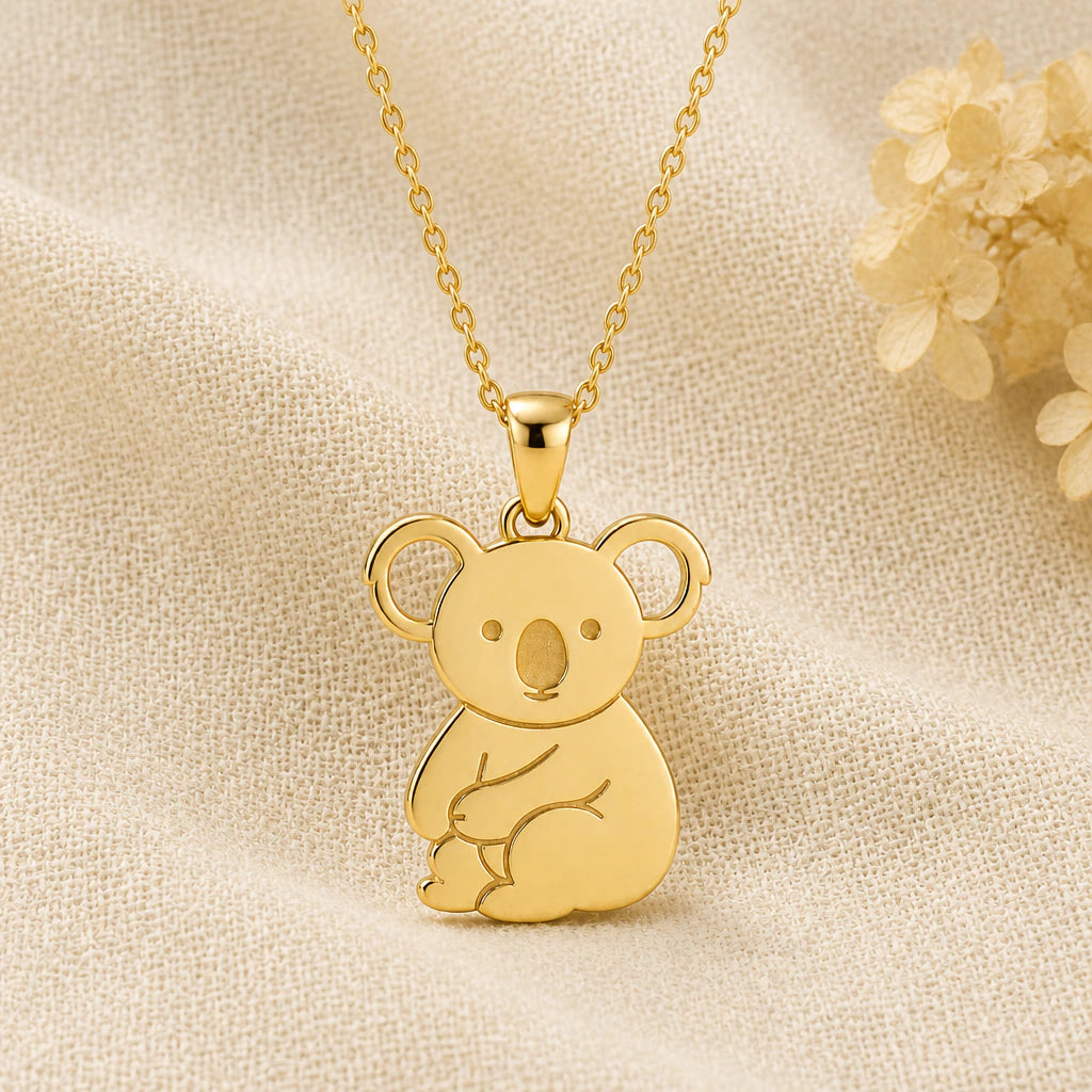 Koala pendant necklace in a warm gold finish on cream fabric