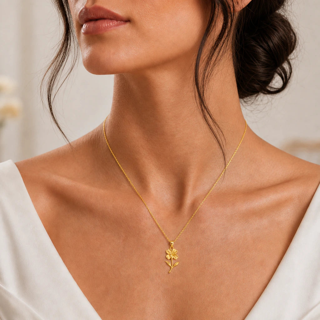 Gold tone impatiens flower pendant necklace worn with a white dress, close-up