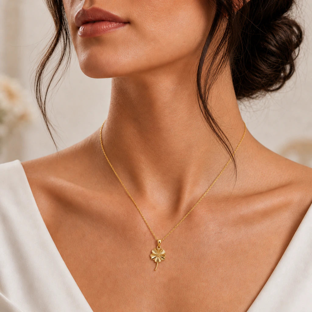 Gold forget me not flower necklace worn with a white V neck dress, close-up